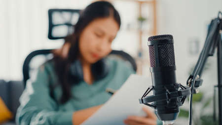 Attractive asia girl record podcast use microphone hold paper creating content for audio blog talk and practice for review topic in her room. Make audio podcast from home,  Sound equipment concept.の写真素材