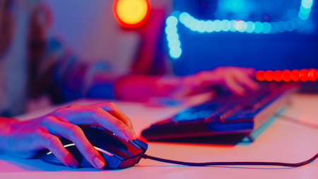 Close-up hands shot asia girl gamer use keyboard and mouse controller play video game with neon light computer in desk at home. Online esport streaming game online, Home quarantine activity concept.の写真素材