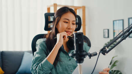 Attractive asia girl record podcast use microphone hold paper creating content for audio blog talk and practice for review topic in her room. Make audio podcast from home,  Sound equipment concept.の写真素材