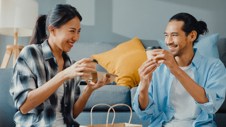 Happy asian young attractive couple man and woman sit at new home drink coffee relax and talk smile with carton package box storage to move in new house. Young married asian move home concept.の写真素材