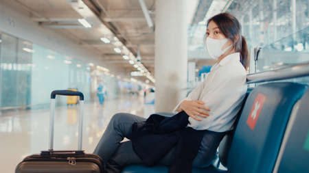 Asian business girl walk with luggage sitting in bench wait and look partner for flight at airport. Business travel commuter covid pandemic, Business travel social distancing, Business travel concept.の写真素材