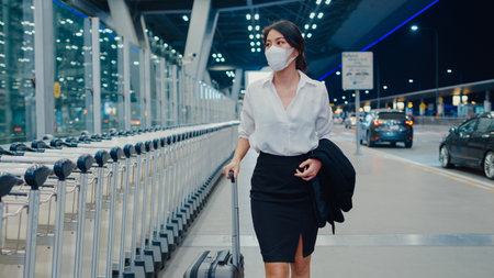 Asian business girl arrive destination wear face mask with drag luggage walk outside wait car terminal at domestic airport. Business commuter covid pandemic, Business travel social distancing concept.の写真素材