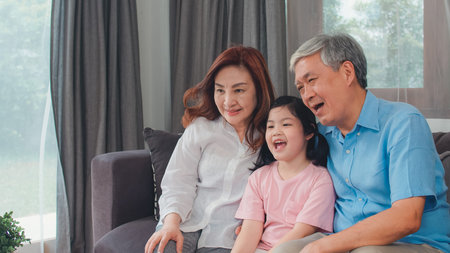 Asian grandparents watch TV with granddaughter at home. Senior Chinese, grandfather and grandmother...