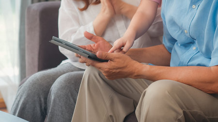 Asian grandparents and granddaughter using tablet at home. Senior Chinese, grandpa and grandma happy...