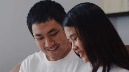 Young Asian Pregnant couple man touch his wife belly talking with his child. Mom and Dad feeling happy smiling peaceful while take care baby, pregnancy lying on sofa in living room at home concept.の写真素材
