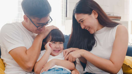 Happy cheerful Asian family dad, mom and daughter having fun cuddling playing on sofa while birthday at house. Self-isolation, stay at homeの写真素材