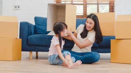 Happy Asian young family homeowners bought new house. Korean Mom and daughter playing together during unpacking in new home after moving in relocation sitting on floor with boxes together.の写真素材