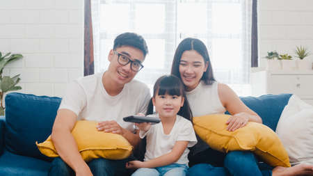 Happy Asian family enjoy their free time relax together at home. Lifestyle Korean dad, mom and daughter watching TV together and having fun lying on sofa in living room in modern house.の写真素材