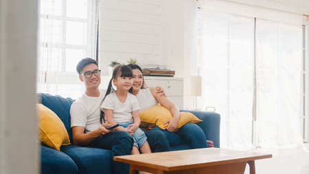 Happy Asian family enjoy their free time relax together at home. Lifestyle Korean dad, mom and daughter watching TV together and having fun lying on sofa in living room in modern house.の写真素材