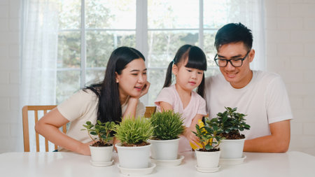 Happy cheerful Asian family dad, mom and daughter watering plant in gardening near window at house. Self-isolation, stay at home, social distancing, quarantine for coronavirus prevention.の写真素材