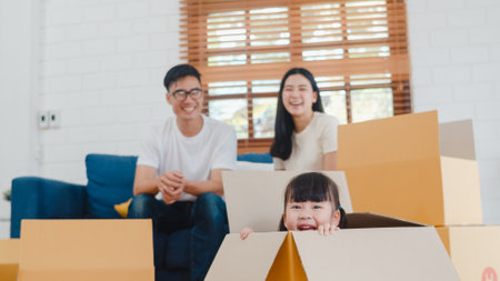 Happy Asian young family homeowners bought new house. Korean Mom, Dad, and daughter playing together during unpacking in new home after moving in relocation sitting on floor with boxes together.の写真素材