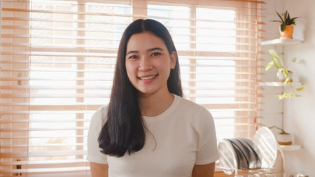 Happy young Asian female feeling happy smiling and looking to camera while relax in kitchen at home. Lifestyle woman at home concept.の写真素材