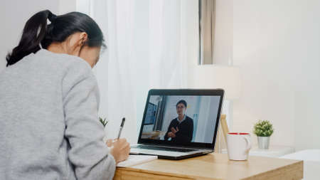 Young Asia teen girl university student using laptop computer distance learning lesson with male teacher remote teaching on internet at home.の写真素材