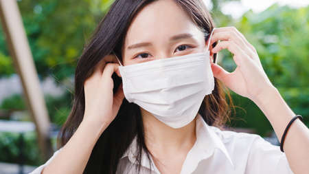 Young Asia businesswoman wear protective face mask looking at camera outsideの写真素材