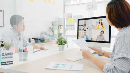Asia business people using desktop talk to colleagues discussing business brainstorm about plan in video call meeting in new normal office. Lifestyle social distancing and work after pandemic.の写真素材