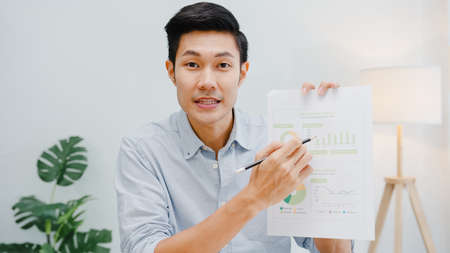 Asia businessman social distancing in new normal situation for virus prevention looking at camera presentation to colleague about plan in video call while work in office.の写真素材