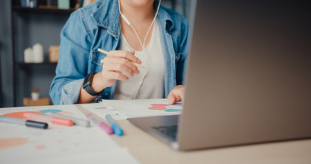 Asia businesswoman using laptop talk to colleagues about plan in video call while working from house at living room. Remotely at workplace, social distancing, quarantine for corona virus prevention.の写真素材