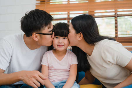 Happy Asian family dad, mom and daughter embracing kissing on cheek congratulating with birthday at house. Self-isolation, stay at home, social distancing, quarantine for virus prevention.の写真素材