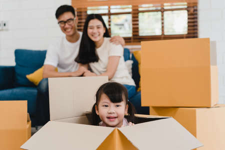 Happy Asian young family homeowners bought new house. Korean Mom, Dad, and daughter playing together during unpacking in new home after moving in relocation sitting on floor with boxes together.の写真素材