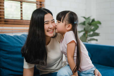 Happy Asian family mom and daughter embracing kissing on cheek congratulating with birthday at house. Self-isolation, stay at home, social distancing, quarantine for coronavirus prevention.の写真素材