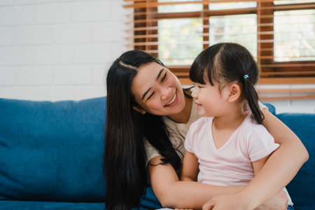 Happy Asian family mom and daughter embracing kissing on cheek congratulating with birthday at house. Self-isolation, stay at home, social distancing, quarantine for coronavirus prevention.の写真素材