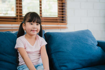 Happy Asian girl enjoy free time relax together at home. Lifestyle Korean child female watching TV together and having fun lying on sofa in living room in modern house.の写真素材