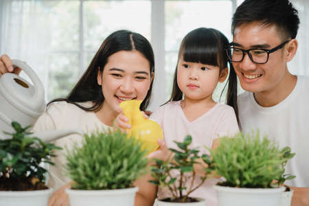 Happy cheerful Asian family dad, mom and daughter watering plant in gardening near window at house. Self-isolation, stay at home, social distancing, quarantine for pandemic prevention.の写真素材