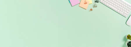 Creative flat lay photo of workspace desk. Top view office desk with keyboard, mouse and book on pastel green color background. Panoramic banner with copy space for text and Advertising area.の写真素材