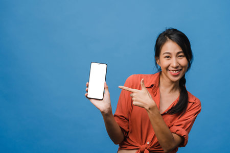 Young Asia lady show empty smartphone screen with positive expression, smiles broadly, dressed in...