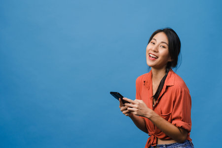 Surprised young Asia lady using mobile phone with positive expression, smile broadly, dressed in...