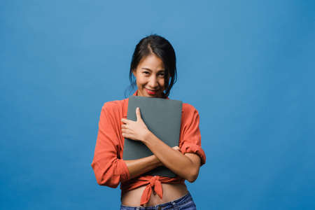 Young Asia lady using laptop with positive expression, smiles broadly, dressed in casual clothing feeling happiness and stand isolated on blue background. Happy adorable glad woman rejoices success.の写真素材