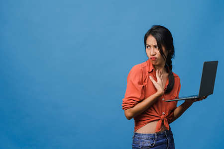 Young Asia lady show empty laptop screen with positive expression, smiles broadly, dressed in casual clothing feeling happiness isolated on blue background. Computer with white screen in female hand.の写真素材