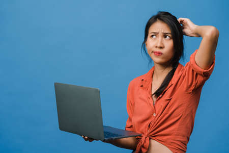 Young Asia lady using laptop with negative expression, excited screaming, cry emotional angry in casual cloth and stand isolated on blue background with blank copy space. Facial expression concept.の写真素材
