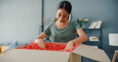 Happy beautiful Asia lady unboxing cardboard delivery package from online marketplace in living room...