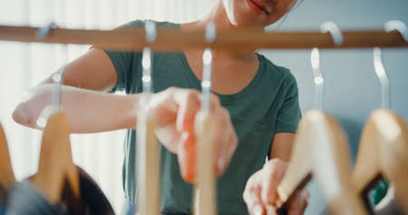Beautiful attractive young Asia lady choosing her fashion outfit clothes in closet living room at house or store. Girl think what to wear casual shirt. Home wardrobe or clothing shop changing room.の写真素材
