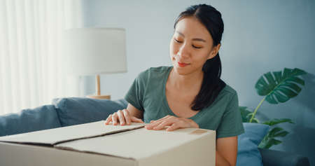 Happy asia lady open cardboard box package exciting and enjoy trying and matching with quality of fashion cloth product from online market in living room at home. Online shopping and delivery concept.の写真素材