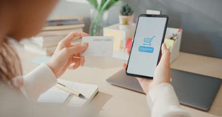 Closeup young asia lady use cellphone order online shopping product and pay bills with credit card in living room interior at house, Self quarantine activity, Fun activity for coronavirus prevention.の写真素材