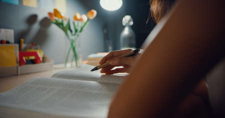 Young Asia teen girl student distance learning lesson and doing homework sitting at desk in living room at house night.の写真素材
