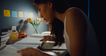 Young Asia teen girl student distance learning lesson and doing homework sitting at desk in living room at house night.の写真素材