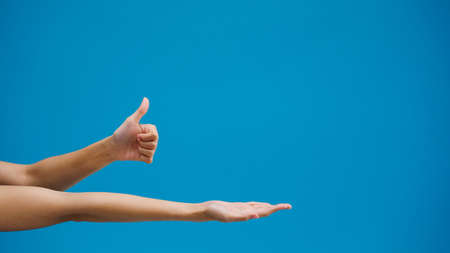 Young girl hand shows something amazing at blank space isolated over blue background in studio. Copy space for place a text, message for advertisement. Advertising area, mock up promotional content.の写真素材