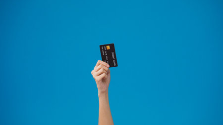 Young woman hand shows credit card for shopping online over blue background in studio. Copy space for place a text, message for advertisement. Advertising area, mockup promotional content.の写真素材