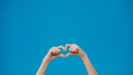 Young woman hand shows making shape of heart sending love to her lover over blue background. Copy space for place a text, message for advertisement. Advertising area, mockup promotional content.の写真素材