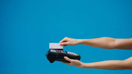 Young girl using credit card into credit card machine or pos terminal blue background in studio. Copy space for place a text, message for advertisement. Advertising area, mockup promotional content.の写真素材