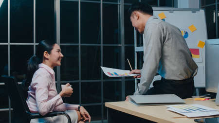 Millennial Asia businessmen and businesswomen meeting brainstorming ideas about new paperwork project colleagues working together planning success strategy enjoy teamwork in small modern night office.の写真素材