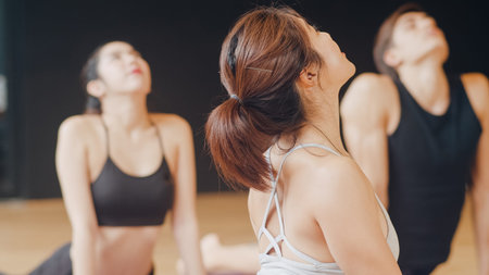 Young diversity sporty people practicing yoga lesson with instructor. Multi racial group of women exercising healthy lifestyle in fitness studio. Sport activity, gymnastics or ballet dancing class.の写真素材