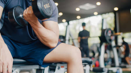 Young athlete Asian guy exercising doing lifting dumbbell fat burning workout in fitness class. Sportsman recreational activity, functional training, people working out, healthy lifestyle concept.の写真素材