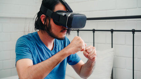 Young Asian man using glasses virtual reality simulator playing boxing game in bedroom, Japanese...