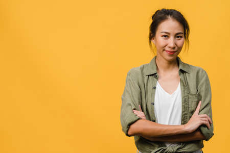 Portrait of young Asia lady with positive expression, arms crossed, smile broadly, dressed in casual clothing and looking at camera over yellow background. Happy adorable glad woman rejoices success.の写真素材