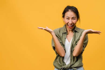 Young Asia lady feel happiness with positive expression, joyful surprise funky, dressed in casual cloth and looking at camera isolated on yellow background. Happy adorable glad woman rejoices success.の写真素材