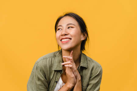 Portrait of young Asia lady with positive expression, smile broadly, dressed in casual clothing over yellow background. Happy adorable glad woman rejoices success. Facial expression concept.の写真素材
